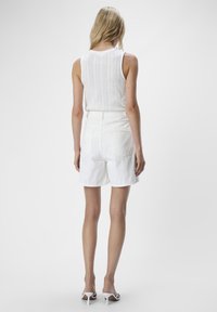 Witte gebreide tanktop met verticale patronen, gecombineerd met hoge witte denim shorts. Het model draagt witte hakken. Eenvoudig, strakke ontwerp.