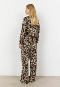 Loungewear-setti leopardikuosisessa ruskeassa ja mustassa. Pitkähihaiset paita ja leveälahkeiset housut, joissa on joustava vyötärö, pehmeällä ja sileällä pinnalla.