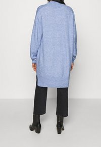 Ljusblå stickad cardigan med lång, lös passform, med ribbad nederkant och ärmslut. Bärs över svarta byxor med klackiga, glansiga stövlar.