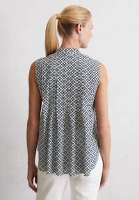Ärmellose Bluse in Hellblau mit einem geometrischen Muster aus gelben und marineblauen Sternen. Ausgestelltes Design mit hohem Ausschnitt und Falten im Rücken.