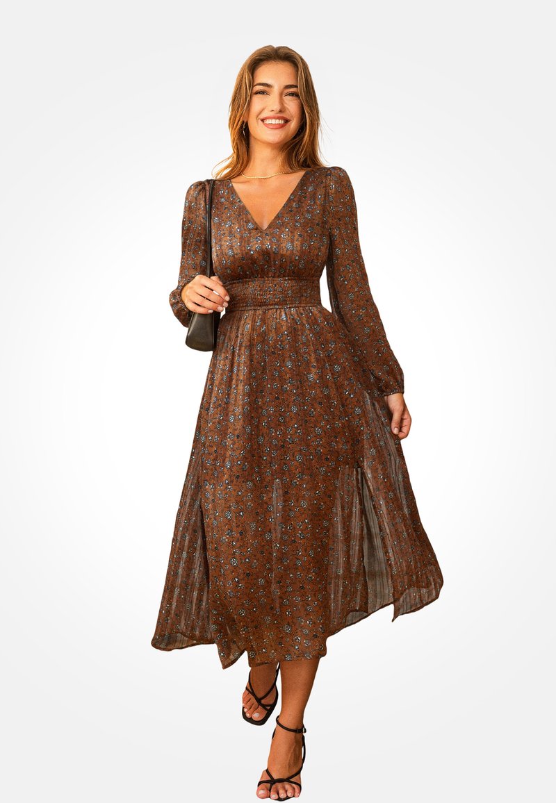 Brązowa maksi sukienka w kwiaty z długim rękawem, dekoltem w kształcie litery V i marszczoną talią. Lekka tkanina z lekko opadającą spódnicą i bocznymi rozcięciami. Czarne sandały.