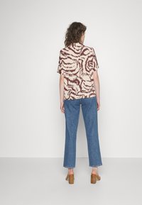 Kortärmad skjorta i krämfärg med ett vinrött abstrakt mönster, tillsammans med blå raka jeans och bruna klacksandaler.