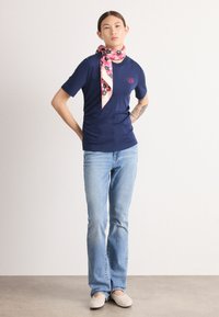 Camicia corta blu navy con sciarpa floreale rosa, jeans a zampa d'elefante blu chiaro e scarpe slip-on beige, con un delicato ricamo sulla camicia.