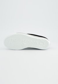 Schwarzer Sneaker von unten gezeigt, mit einer weißen Sohle, die mit strukturierten Punkten versehen ist, und "paul green" ist im Profil eingeprägt.