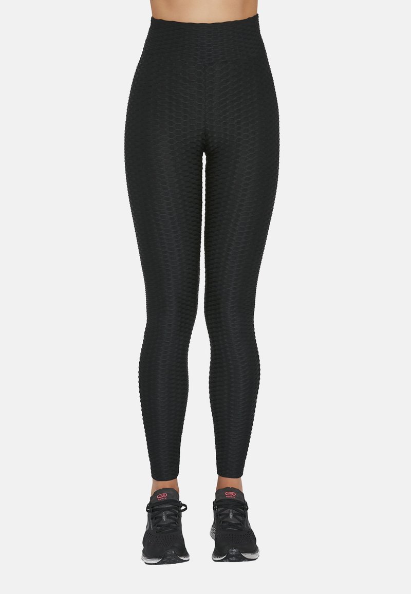 Czarne legginsy z wysokim stanem wykonane z fakturowanej tkaniny o wzorze plastra miodu, zestawione z czarnymi butami sportowymi z różowymi akcentami.