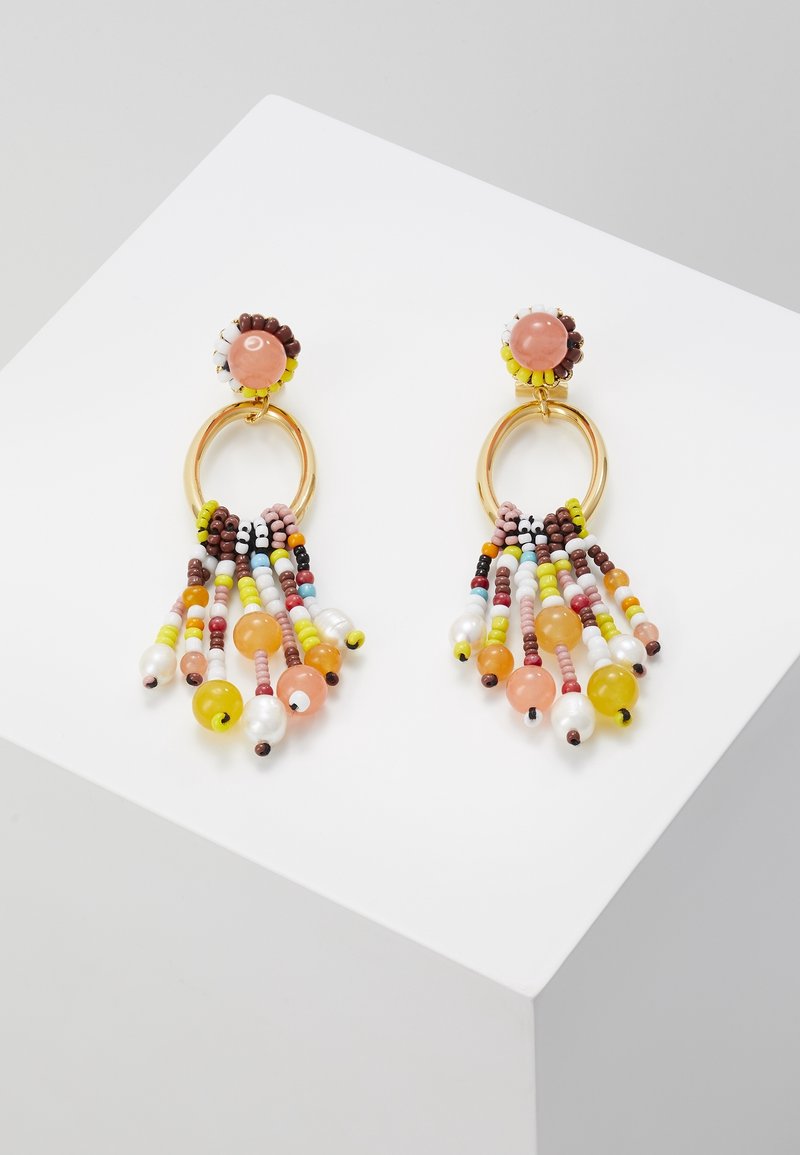 Paire de créoles dorées avec des perles multicolores et des brins pendants jaune, rose, marron, blanc et orange, exposées sur une surface blanche.
