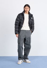 Svart pufferjacka med hög krage, krämfärgad t-shirt, grå cargobyxor och beige sneakers med svarta ränder. Släta och vadderade texturer.