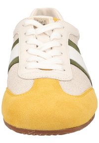 Vue de face d'une chaussure de sport décontractée avec des lacets blancs, un bout en daim jaune, une tige en tissu beige, et des bandes latérales vertes et blanches.