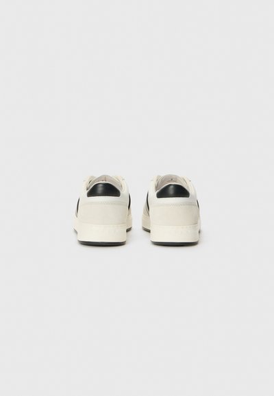 White leather sneakers with black suede accents, round toe, and rubber sole. Features minimal branding on the heel and textured material.