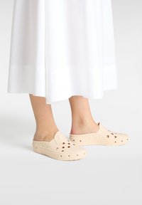 Sabots slip-on beiges fabriqués en matériau léger et durable ; dotés de trous de ventilation, d'un bout arrondi et d'un design profil bas.