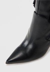 Bottines noires en cuir avec un bout pointu. Elles présentent une texture lisse et un design épuré, accentué par un détail de panneau latéral.