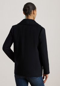 Czarny wełniany płaszcz z klapowym kołnierzem, o strukturalnym kształcie i czystym designie. Posiada długie rękawy oraz pojedynczy szew z tyłu.