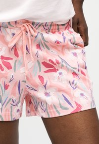 Κοντινή λήψη ατόμου που φοράει ροζ σορτσάκι με λουλουδάτο σχέδιο, με κορδόνι στη μέση και λευκό τοπ που είναι μερικώς ορατό.