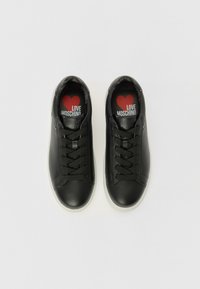 Baskets en cuir noir avec bout rond, lacets plats et semelle en caoutchouc blanche. L'intérieur présente un logo en forme de cœur rouge avec le texte "LOVE MOSCHINO".