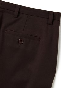 Close-up van donkerbruin op maat gemaakte broek met een knoopzak aan de achterkant en riemlussen op de taille.