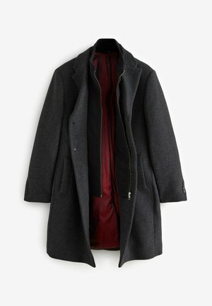 Cappotto di lana grigio scuro con revers a punta e due tasche frontali; presenta una fodera interna color bordeaux e una superficie esterna liscia.