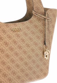 Borsa a spalla in tessuto marrone con motivo a logo in rilievo, hardware dorato e un portachiavi decorativo. Presenta una forma strutturata e apertura superiore.