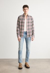 Cotton plaid shirt in red, navy, and yellow; long sleeves, button-down collar. Worn with light blue distressed jeans and brown slip-on shoes.