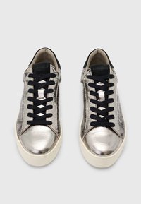 Un paio di sneakers low-top in argento metallico con lacci neri e suole spesse bianche, viste dall'alto su uno sfondo grigio.