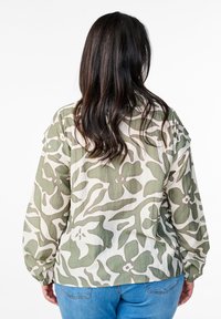 Long-sleeve shirt with a floral green and cream print, textured fabric, and elastic cuffs, paired with blue jeans.