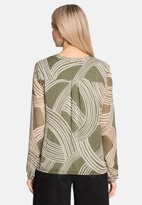 Transparente Langarmbluse in Olivgrün mit weißem Wellenmuster und dezenten goldenen Akzenten. Plissee-Detail auf der Rückseite sorgt für Textur.