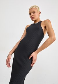 Black ribbed tank dress with a fitted silhouette, high neckline, and side cutouts. Smooth texture and minimal design elements.