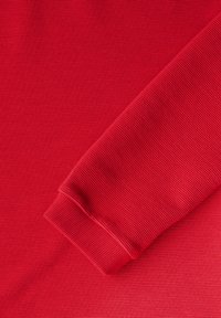 Roter gerippter Stoff mit einem gefalteten Ärmel und einem strukturierten Muster. Glatte Oberfläche mit einer leicht elastischen Qualität.