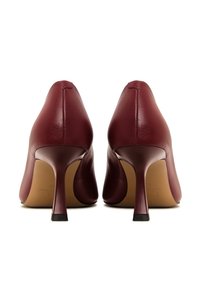 Tacchi alti in pelle borgogna con punta affusolata e sottile tacco a stiletto. Texture liscia e design minimalista, con un accento in gomma nera alla base del tacco.