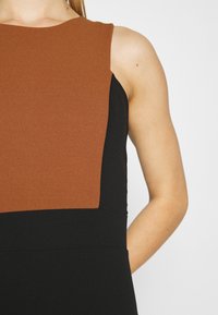 Robe sans manches avec un design bicolore, haut marron et bas noir. Confectionnée dans un tissu doux avec une silhouette structurée.