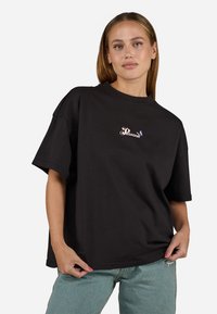 Black t-shirt made of cotton, featuring a crew neck and short sleeves. Front has colorful "Pegador" logo with accents. Relaxed fit.
