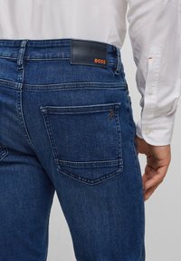 Mörkblå jeans i denim med en snygg design, utrustade med en läderlapp märkt "BOSS" och två bakfickor med subtil sömnad.