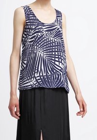 Bezrukávý top v bílé barvě s modrým vzorem palmových listů; měkká tkanina; volný střih; kulatý výstřih; v kombinaci s černou sukní.