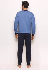 Men's loungewear set featuring a blue long-sleeve shirt with ribbed cuffs and navy cotton pants with elasticated ankles.