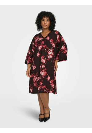 Robe noire avec un motif floral rose, longueur genou, coupe ample, décolleté en V et manches trois-quarts. Portée avec des talons noirs en cuir verni.