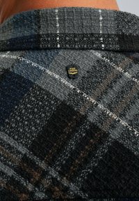 Grijs en zwart geruite stof van een overhemd met een gestructureerde afwerking. Bevat een klein logo etiket bij het kraaggebied.