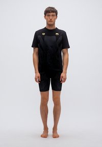 Μαύρο αθλητικό σετ που περιλαμβάνει μια μπλούζα με στρογγυλή λαιμόκοψη, υφασμένο μοτίβο και χρυσές λεπτομέρειες, σε συνδυασμό με εφαρμοστά σορτς που ταιριάζουν.