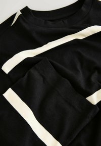 Mustast puuvillast T-särk, mille esiküljel ja varrukal on valged diagonaaltriibud. Pehme tekstuuriga, ümara kaelusega ja standardsuuruses lõige.