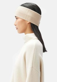 Beige ribbad stickad hårband gjort av mjukt tyg, bred design, bärs ovanför axellångt rakt hår, med en subtil textur och sömlösa kanter.