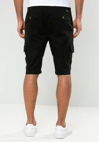 Schwarze Cargo-Shorts mit mehreren Taschen und einer figurschmeichelnden Passform, aus einem strapazierfähigen Stoff. Getragen mit weißen Sneakern, von hinten betrachtet.