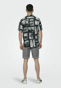 Camisa de manga corta en blanco y negro que presenta un collage de fotos; combinada con pantalones cortos grises y zapatillas blancas.