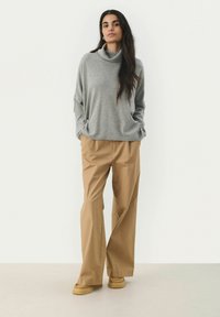 Pulover gri cu guler înalt, croială relaxată, asortat cu pantaloni lejerați de culoare bej. Textură moale, design minimal, potrivit pentru ținute casual.