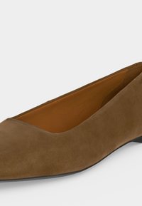 Chaussure plate pointue en daim marron avec petit talon et doublure intérieure beige présentée sur fond blanc.