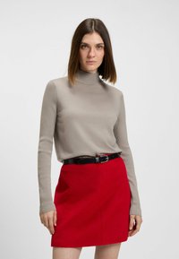 Beige pitkähihainen neulepaita, jossa on ribbipinta, yhdistetty punaisen mini-hameen kanssa, jossa on musta vyö. Kiinnitä huomiota väreihin ja materiaaliin.