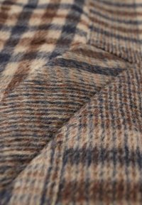 Tejido de lana con un patrón de cuadros marrón y beige, con acentos en azul oscuro. Textura suave con grosor variable y diseño entrelazado.