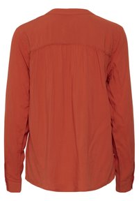 Camicia a maniche lunghe color arancio bruciato, realizzata in un tessuto morbido. Presenta un orlo curvo e dettagli arricciati sulla parte posteriore della spalla. Polsini con bottoni.