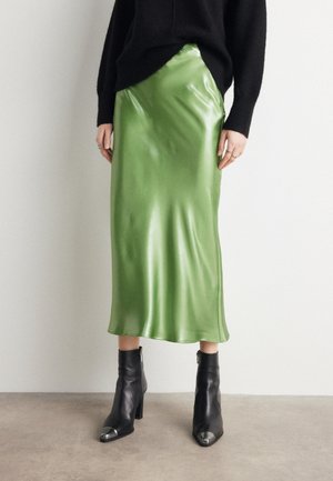 Grønn sateng midi-skirt med en jevn, glanset tekstur, parret med svarte ankelstøvler med sølv tåhette og glidelåser.