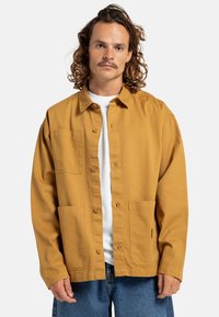 Lange mouwen, mosterdgele overhemdjas van katoen, met een knoopsluiting aan de voorkant, twee voorzakken en een relaxte pasvorm.
