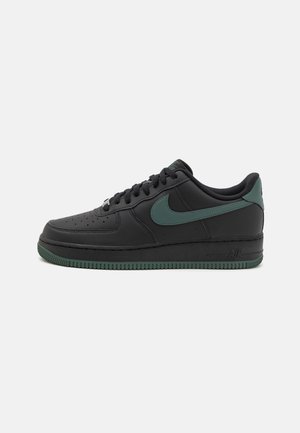 Baskets basses noires avec logo Nike swoosh vert foncé, semelle extérieure verte assortie et lacets noirs sur fond blanc.