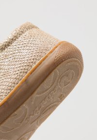 Goldfarbene, texturierte Slipper mit flexiblem Gummisohle und gemustertem Design. Die Oberfläche hat einen subtilen Glanz und eine abgerundete Zehenpartie.
