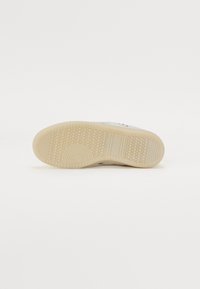 Suola della scarpa, materiale in gomma, colore beige chiaro con un motivo a nido d'ape testurizzato, caratterizzata da scanalature circolari e orizzontali per una maggiore aderenza.